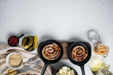 Wurst or Bratwurst with Fermented Cabbage, Pickled Cucumber, and Spices in cast iron frying pan, on white background, top view flat lay, with space for text copyspaceの写真素材