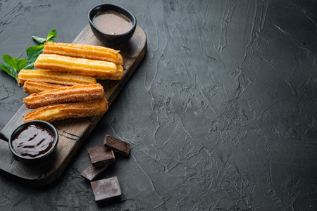 Traditional Spanish dessert churros with sugar and chocolate set, on black background with space for...