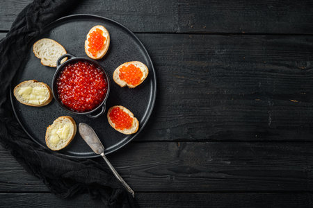 Bruschette with butter red caviar, on black wooden table background, top view flat lay with copy...