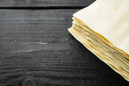Dried uncooked lasagna pasta sheets set, on black wooden table background, with copy space for text