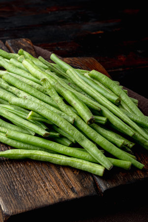 Green string bean set, on wooden cutting board, on old dark wooden table background