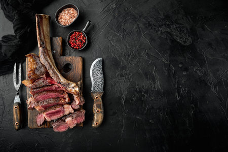 Medium rare dry aged beef steak grilled and sliced set, tomahawk cut, on wooden serving board, on black stone background, top view flat lay, with copy space for textの写真素材