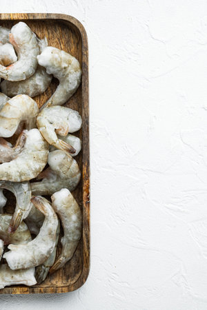 Frozen raw uncooked tiger prawns, shrimps set, on wooden tray, on white stone surface, top view flat...