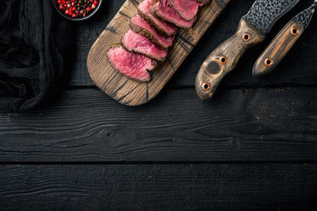 Medium rare dry aged beef steak grilled and sliced set, tenderloin or fillet mignon cut, on wooden serving board, on black wooden table background, top view flat lay, with copy space for textの写真素材