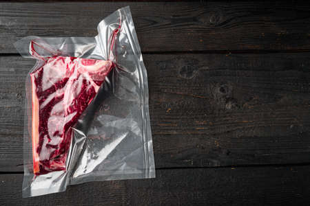 T-or florentine dry aged raw bone marbled beef steak in vacuum packaging set, on black wooden background, top view flat lay, with copy space for textの写真素材