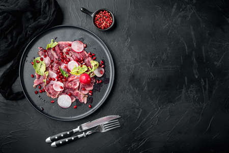 Beef Carpaccio cold appetizer set, with Radish and garnet, on plate, on black stone background, top view flat lay, with copy space for textの写真素材