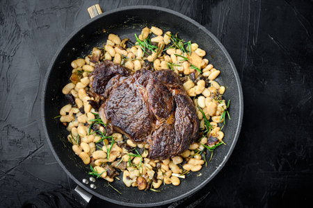 Grilled marbled beef meat rib eye steak and vegetables set, on frying cast iron pan, on black stone background, top view flat lay, with copy space for textの写真素材