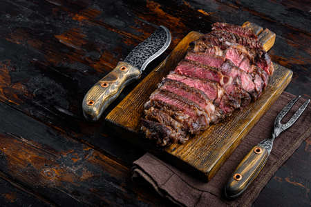 Fresh grilled meat. Grilled beef steak medium rare set, rib eye cut, on wooden serving board, on old dark wooden table background, with copy space for textの写真素材
