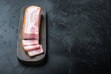 Bacon pancetta cut and sliced on black background with space for text.の写真素材