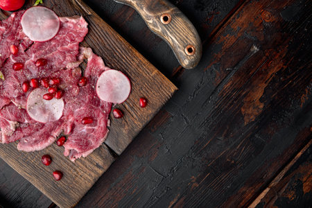 Delicatessen appetizer of fresh marbled meat - beef carpaccio set, with Radish and garnet, on wooden serving board, on old dark wooden table background, top view flat lay, with copy space for textの写真素材