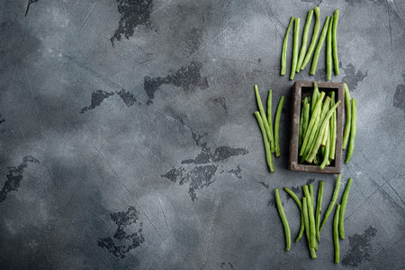Fresh green French beans set, in wooden box, on gray stone background, top view flat lay, with copy...