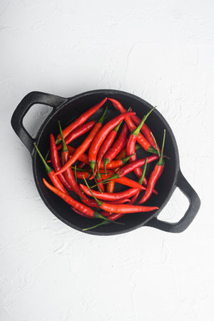 Chili spur pepper set, in frying cast iron pan, on white stone background, top view flat lay, with...