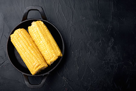 Delicious juicy sweet boiled corn set, on black stone background, top view flat lay, with copy space...