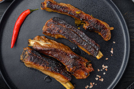 Pork ribs grilled with BBQ sauce and caramelized in honey set, on plate, on black wooden table background, top view flat layの写真素材