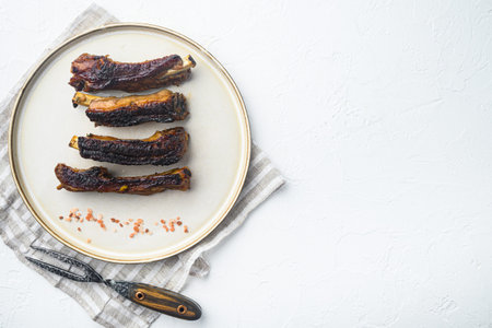 Spicy hot grilled spare ribs from a summer BBQ set, on plate, with barbeque knife and meat fork, on...