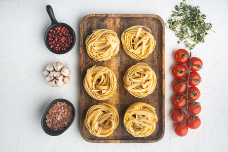 Raw pasta tagliatelle with fresh tomatoes and herbs set, on white stone background, top view flat layの写真素材