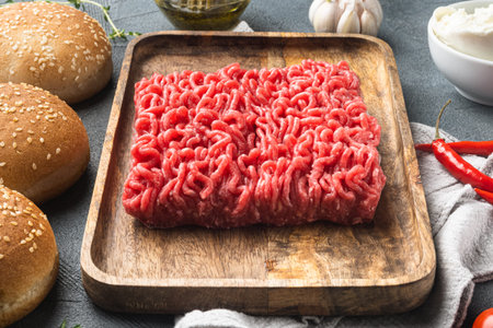 Fresh raw minced beef meat for meatball burgers with sesame buns set, on wooden tray, on gray stone...