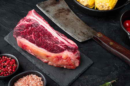 Black angus dry aged club steak with herbs and seasoning set, on black stone background