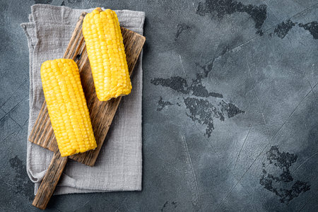 Boiled sweet corn cobs with butter set, on gray stone background, top view flat lay, with copy space...