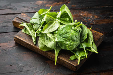 Bundle of fresh spinach set, on wooden cutting board, on old dark wooden table backgroundの写真素材