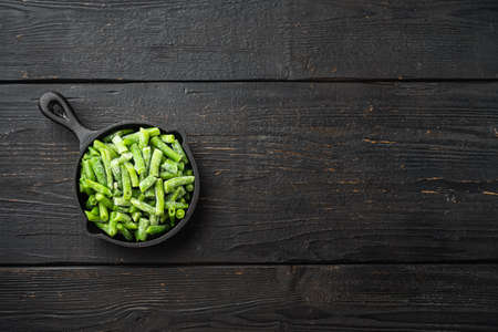 Bright juicy frozen green beans set, in frying cast iron pan, on black wooden table background, top view flat lay, with copy space for textの写真素材