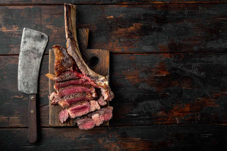 Sliced barbecued tomahawk rib tip with rosemary, salt and herbs medium rare set, on wooden serving board, on old dark wooden table background, top view flat lay, with copy space for textの写真素材