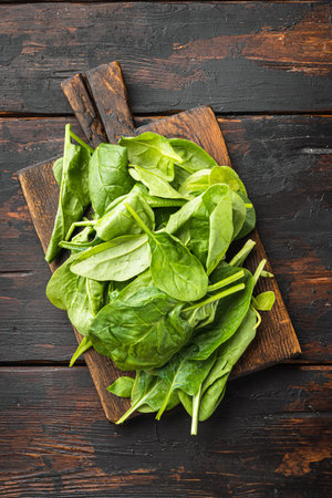 Fresh spinach leaves set, on wooden cutting board, on old dark wooden table background, top view...
