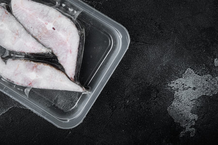 Halibut fish frozen steak pack set, on black dark stone table background, top view flat lay, with...