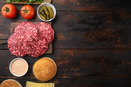 Ingredients for cooking burgers. Minced beef patties, buns, tomatoes, herbs and spices set, on old dark wooden table background, top view flat lay, with copy space for textの写真素材
