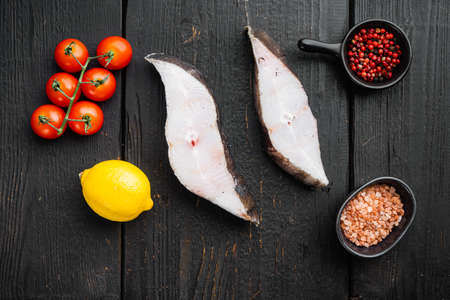 Piece of fresh raw halibut fish set, with ingredients and rosemary herbs, on black wooden table background, top view flat lay, with copy space for textの写真素材
