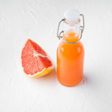 Fresh grapefruits and glass of grapefruit juice set, square format, on white stone table backgroundの写真素材
