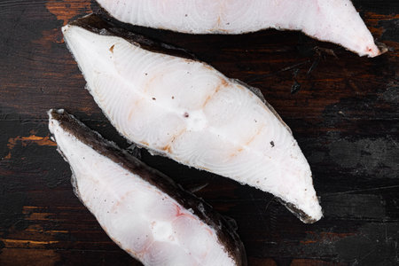 Frozen fillets of white fish, pollock set, on old dark wooden table background, top view flat lay