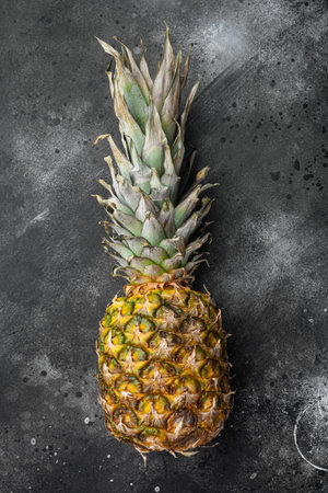 Single whole pineapple set, on black dark stone table background, top view flat lay, with copy space...