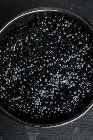 Black bowl of black caviar, on black background, top view flat lay