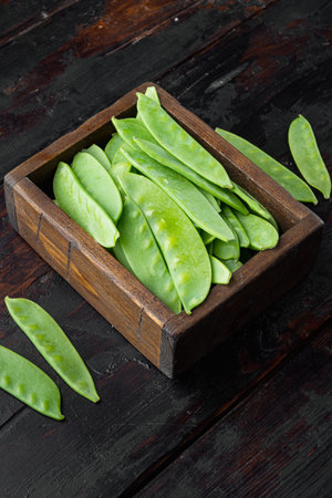 Sugar snap peas, raw ripe baby pods set, in wooden box, on old dark wooden table background