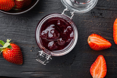 Small glass bowl, of red berry jam, on black wooden table background, top view flat lay