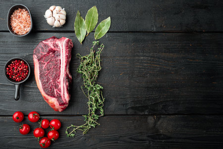 Raw club steak with ingredients set on black wooden table background, top view flat lay, with copy space for textの写真素材