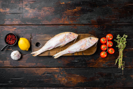 Raw fresh mullet or barabulka whole fish set, with ingredients and herbs, on old dark wooden table...