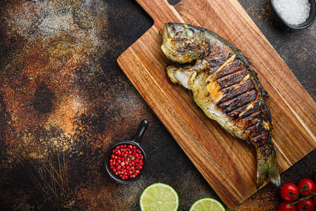 Grilled sea bream or dorado raw fish on chopping board with ingredients over old metall dark background, top view with space for textの写真素材