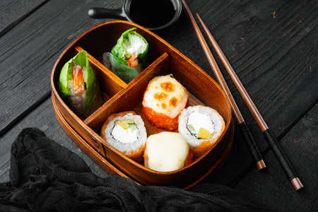 Japanese Meal in a Box Bento with sushi roll eice avocado salmon fish set, on black wooden table backgroundの写真素材