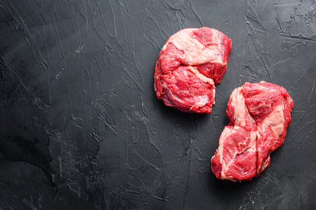 Raw chuck eye roll steak cuts, top view on black textured background with space for text