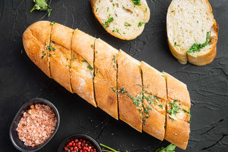 Sliced grilled bread with garlic and herbs set, on black dark stone table background, top view flat layの写真素材