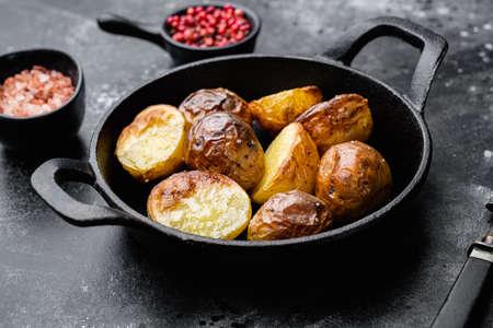 Baked potatoes with herbs and garlic set, in frying cast iron pan, on black dark stone table backgroundの写真素材