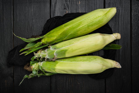 Ear of maize or corn, on black dark stone table background, top view flat lay