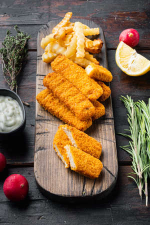 Pile of golden fried fish fingers with white garlic sauce set, on wooden cutting board, on old dark wooden table backgroundの写真素材