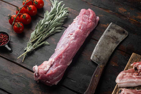Raw pork fillet tenderloin. Fresh meat with ingredients and herbs for grill or baking, sage, potatoe set with old butcher cleaver knife, on old dark wooden table backgroundの写真素材