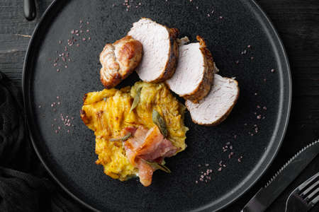 Baked pork fillet loin with potatoe and herbs set, on plate dish, on black wooden table background, top view flat layの写真素材