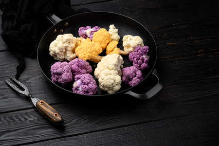 Organic colorful cauliflowers set, on frying cast iron pan, on black wooden table backgroundの写真素材