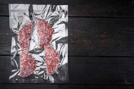 Beef veal cutlets in vacuum plastic pack set, on black wooden table background, top view flat lay, with copy space for textの写真素材