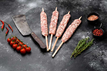Raw Lula kebab on skewers set, with grill ingredients, on black dark stone table background, with copy space for textの写真素材